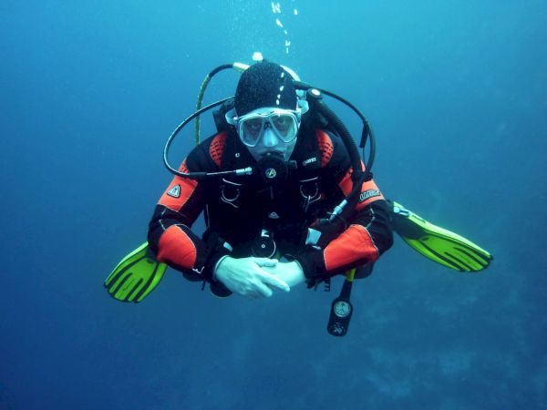 A scuba diver wearing a red wetsuit and full gear, bright yellow fins, and a mask, underwater with hands folded in front, bubbles rising.
