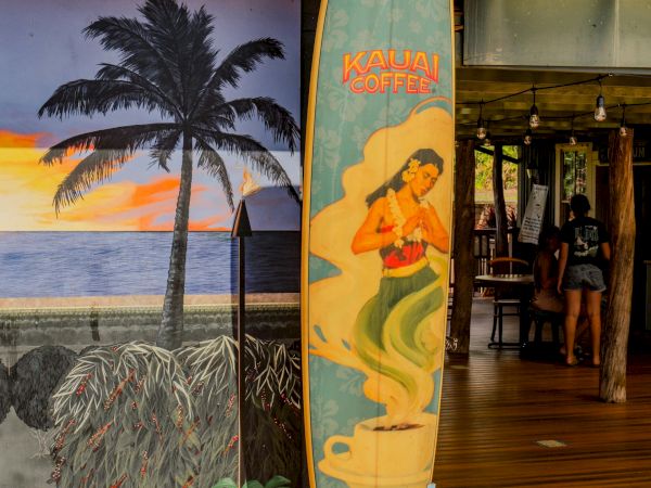 A tropical scene with a painted surfboard leaning against a seaside building, palm tree mural, and wooden deck.