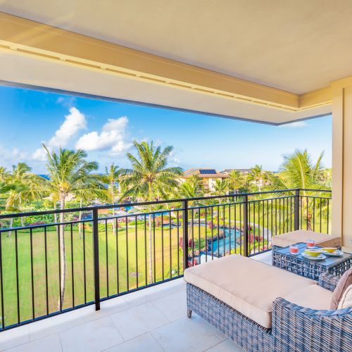 A balcony with wicker loungers overlooks a sunny landscape with palm trees and clear skies.
