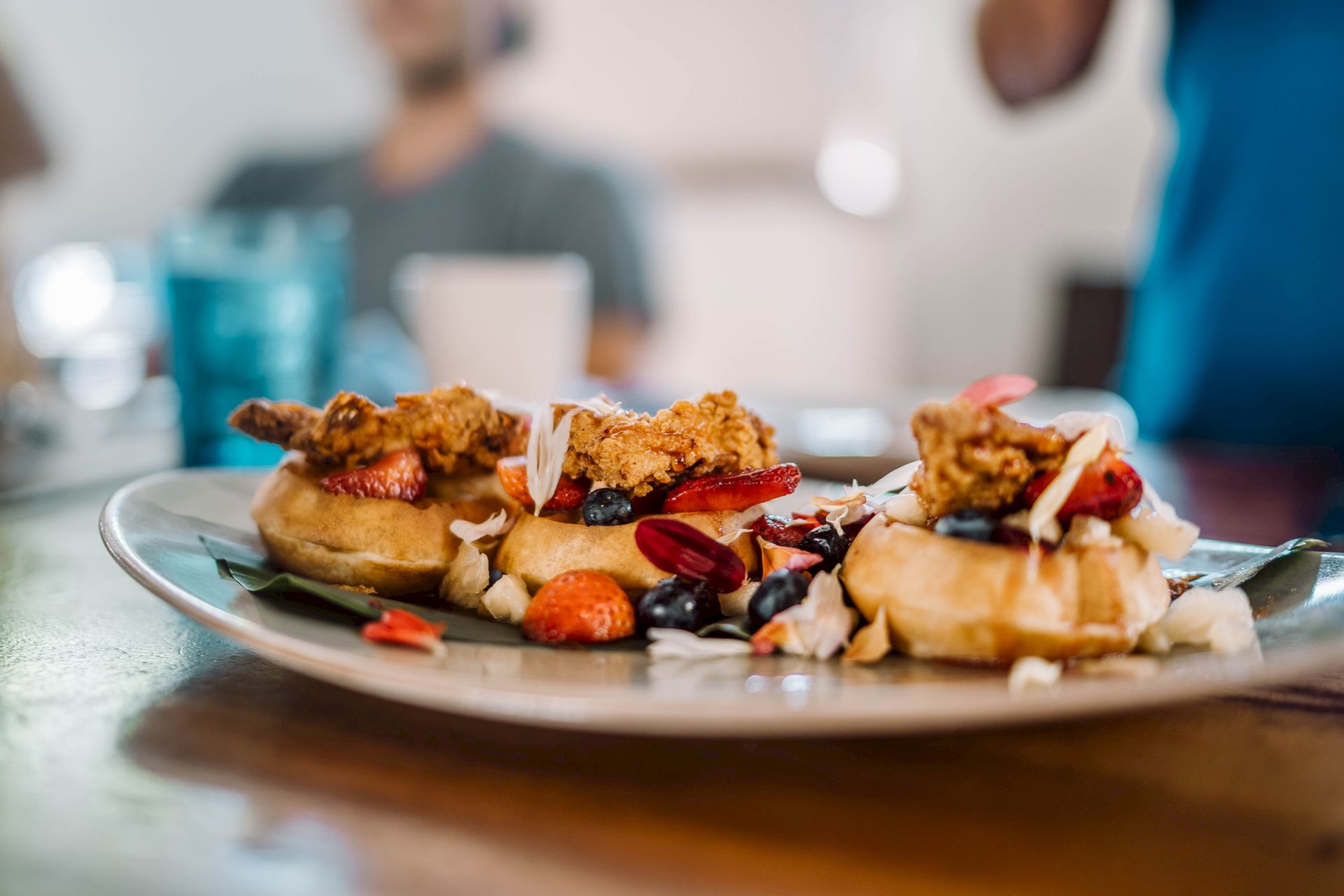 A close-up of a plate with crispy chicken nuggets, bread, and fruit/veggies, with a person blurred in the background.