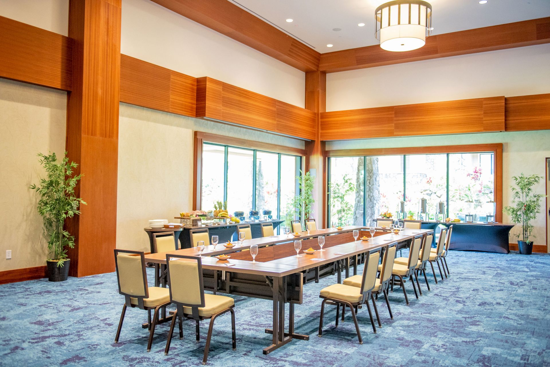 Bright modern meeting room with a long table, upholstered chairs, blue carpet, and large windows.