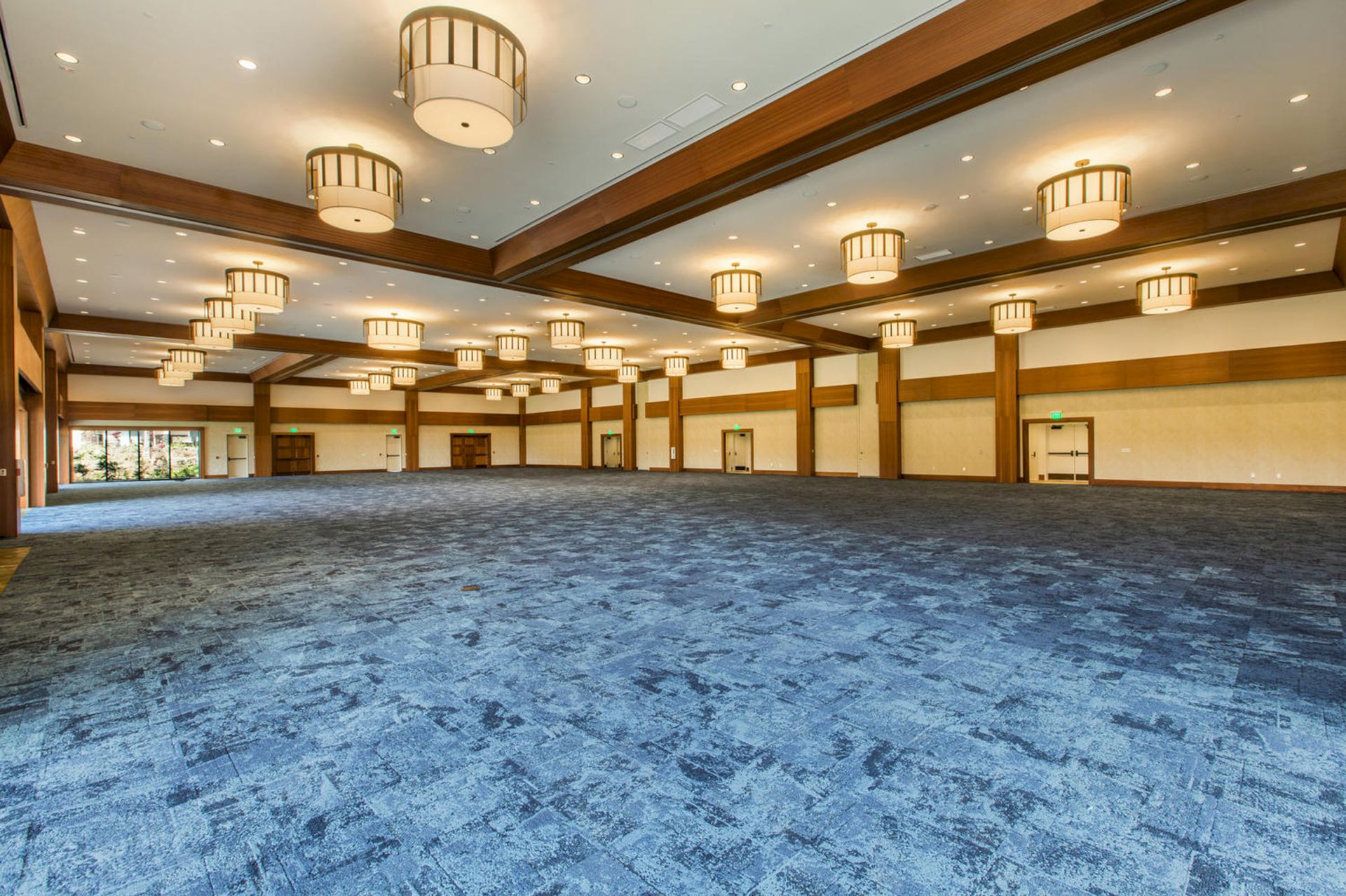 A spacious indoor hall with blue carpet, wood paneling, and many cylindrical pendant chandeliers lighting the room.