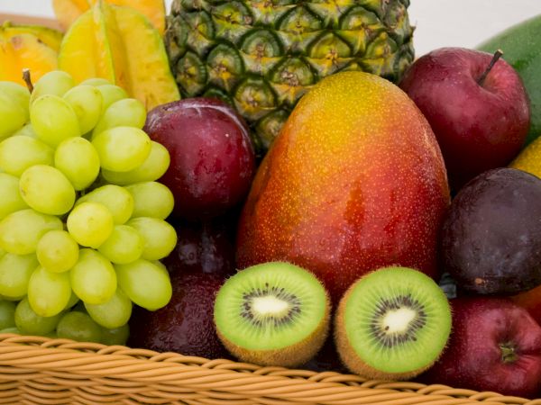 A colorful fruit basket with pineapple, grapes, kiwis cut in half, mango, apples, mangoes, and other tropical fruits.