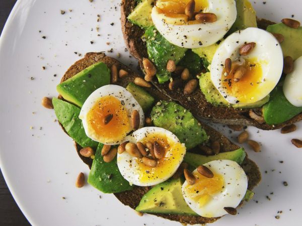 A plate of avocado toast topped with sliced hard-boiled eggs, greens, seeds, and a drizzle of sauce&mdash;salty, crunchy, and fresh.