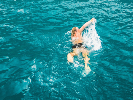 A person is swimming in a large body of water, with splashes around them, under clear blue skies.
