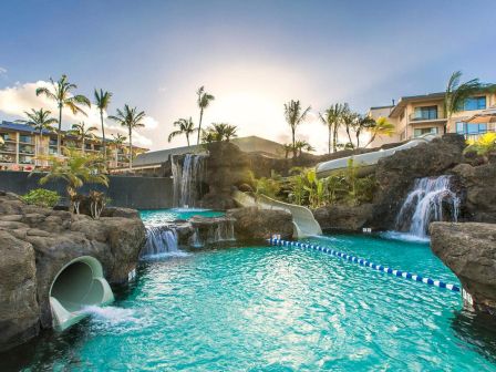 A luxurious tropical resort pool with turquoise water, rock slides, waterfalls, palm trees, and sunlit villas in the background. End.