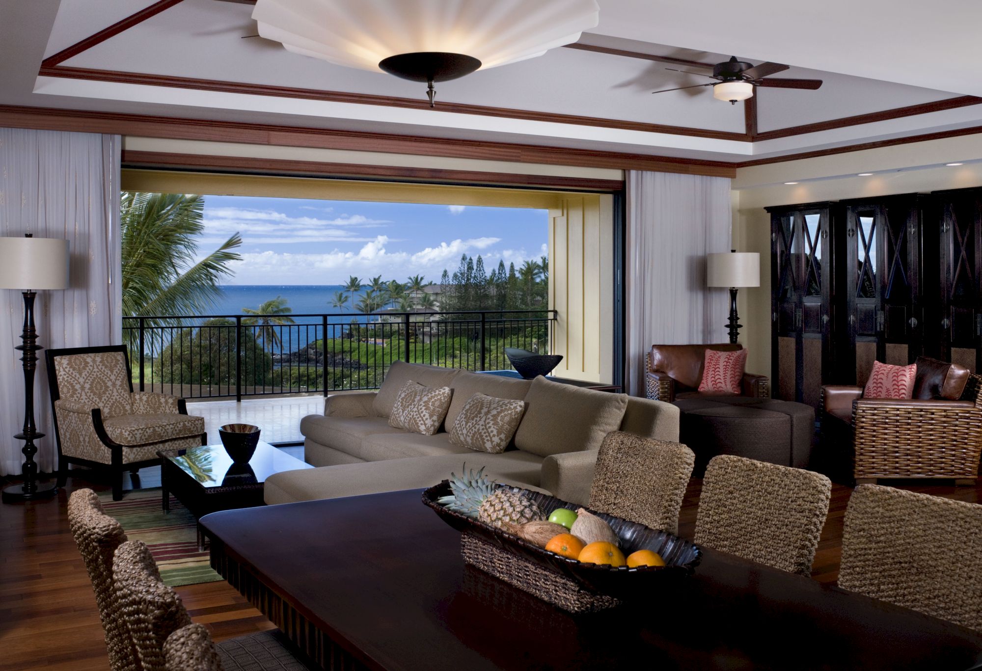 A bright living room with a sofa, ceiling fan, and ocean view through large open windows.
