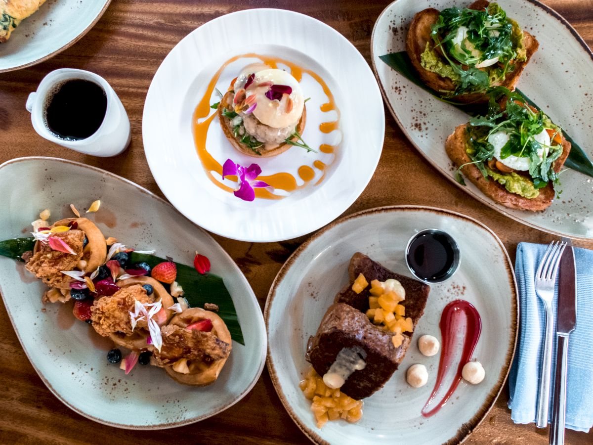 Gourmet open-faced toasts with greens and creamy toppings, served with black coffee on colorful plates, plus garnished sides.
