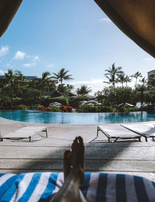 A sunny resort pool with lounge chairs, palm trees, and villas under a blue sky, creating a tropical getaway vibe.