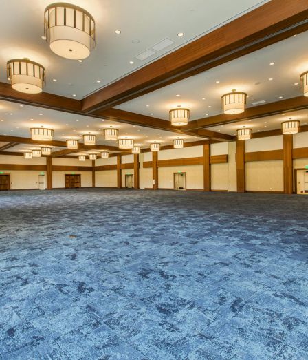 An empty, spacious hall with a blue stone-style floor, wood-trimmed ceiling beams, and many round pendant lights glowing overhead.