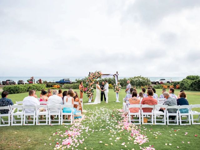 An outdoor beach wedding ceremony with guests seated on white chairs, exchanging vows under a floral arch near the ocean.
