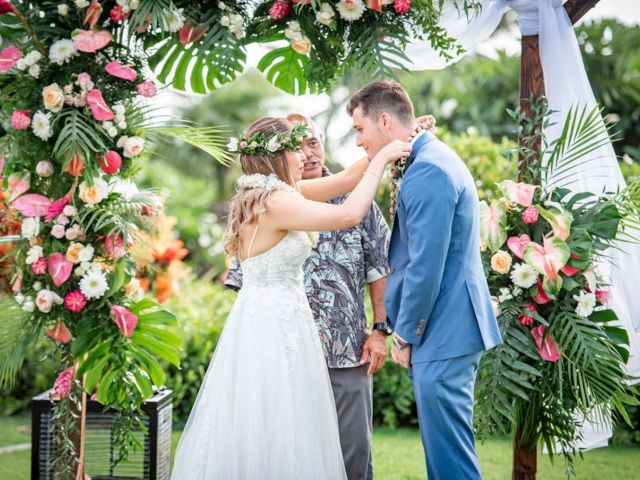 A bride and groom under a floral garden arch share a tender moment at an outdoor wedding.