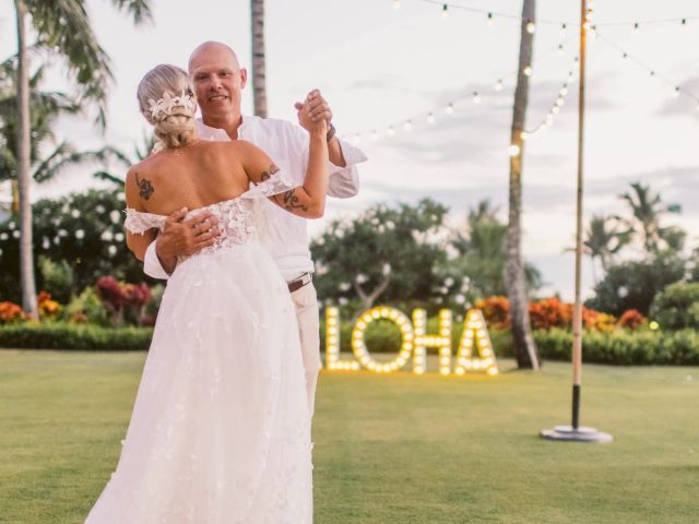 A bride and groom in wedding attire dance outdoors at a garden event with string lights and an illuminated &ldquo;OHANA&rdquo; sign.